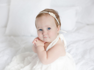 baby girl in white dress sitting on white bed during her one year portrait session by Rhonda Cunningham Photography, Lexington Ky baby photographer