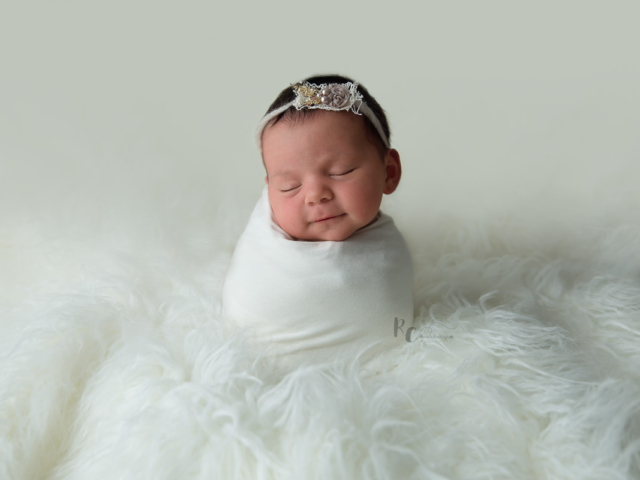Newborn portrait of baby swaddled and sitting upright in cream fur by Lexington Ky Newborn Photographer Rhonda Cunningham Photography.