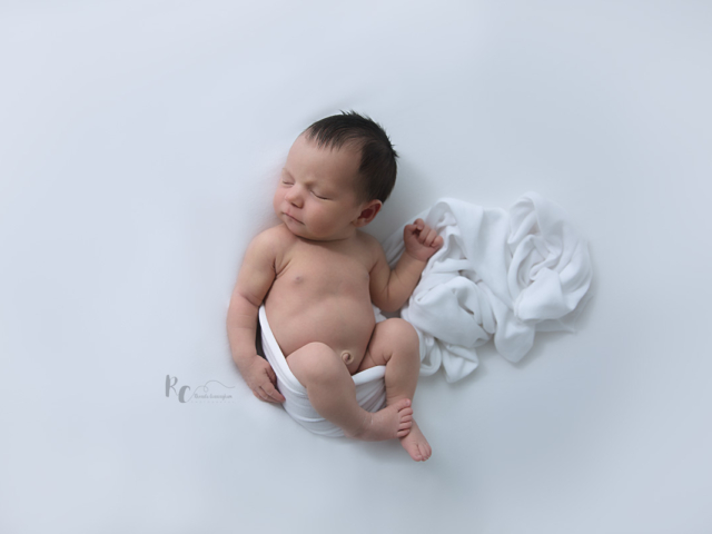 Newborn baby in a simple white set up on a white backdrop with a white wrap around baby. Captured by Rhonda Cunningham Photography, Lexington Ky newborn photographer.