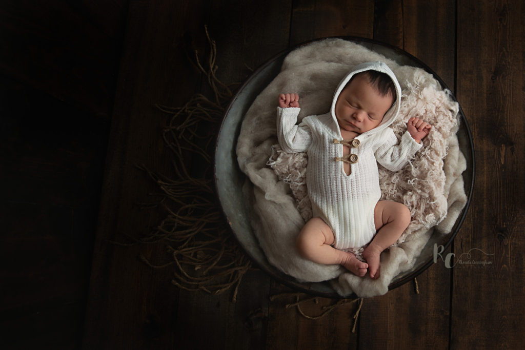 Rustic newborn portrait by Rhonda Cunningham Photography, Lexington Ky newborn photographer. Image is of baby in hoodie outfit laying in rustic bowl.