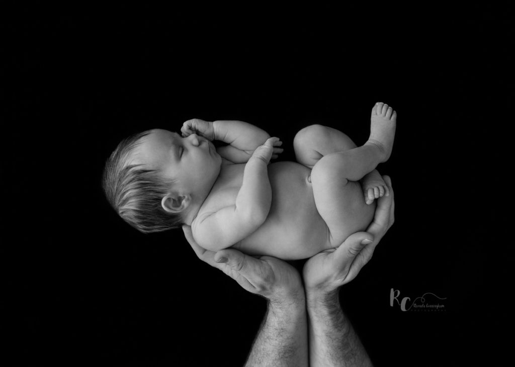 Black and white image of dad's hands holding newborn. Captured by Rhonda Cunningham Photography, Lexington Ky newborn photographer